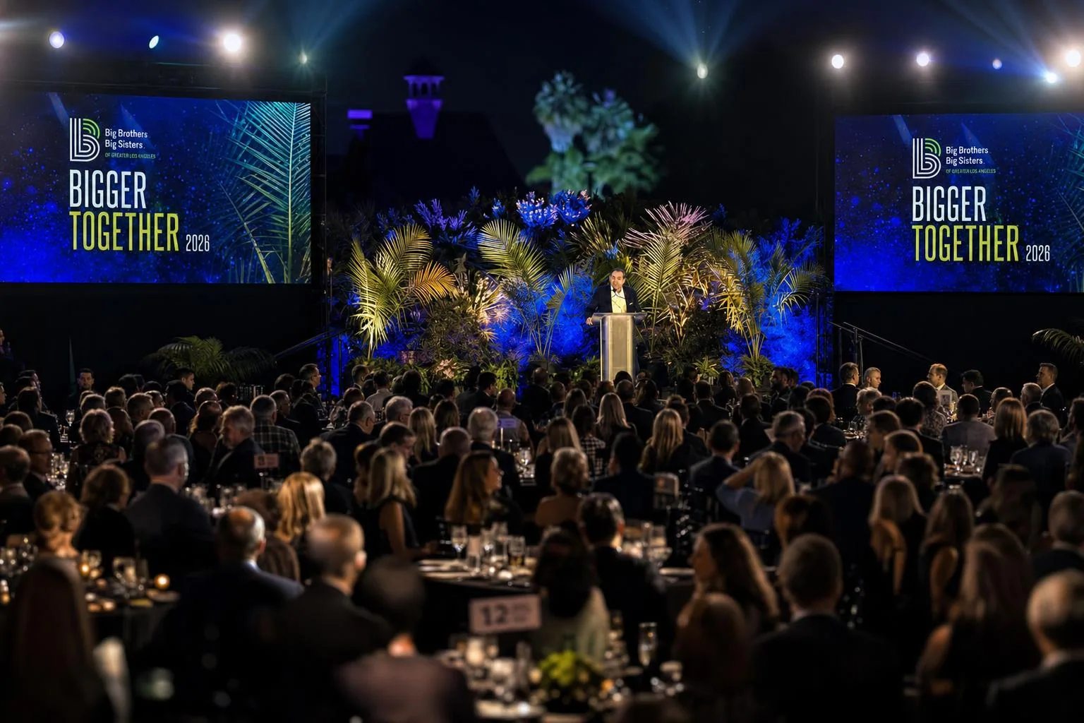 Keynote speaker on stage at a gala with flashy dual LED screens showing cinematic motion-graphics branding
